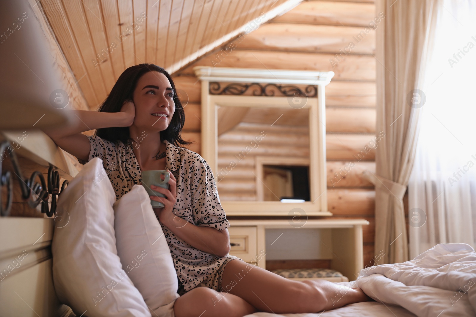 Photo of Young woman in pajamas with drink on bed at home. Lazy morning