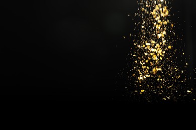 Photo of Shiny golden glitter falling down on black background, space for text. Bokeh effect