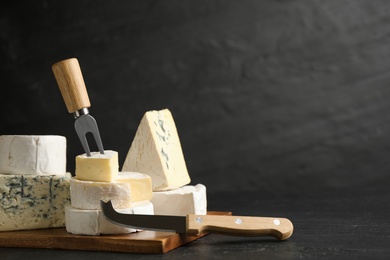 Photo of Different types of cheese, knife and fork on black table. Space for text