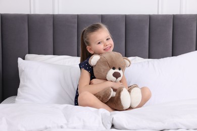 Photo of Cute little girl playing with teddy bear on bed