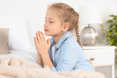 Photo of Girl with clasped hands praying near bed at home