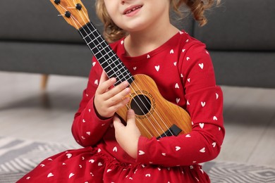 Little girl playing toy guitar at home, closeup