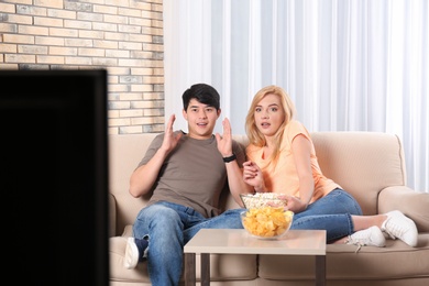 Young couple with snacks watching TV on sofa at home
