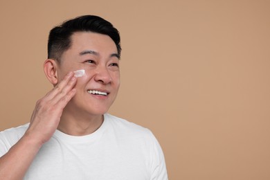 Handsome man applying cream onto his face on light brown background. Space for text