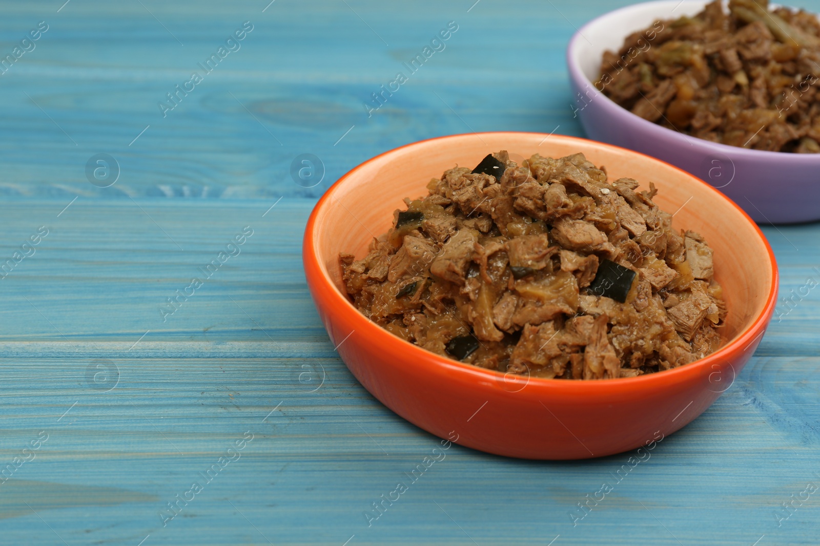 Photo of Wet pet food in feeding bowl on light blue wooden table. Space for text