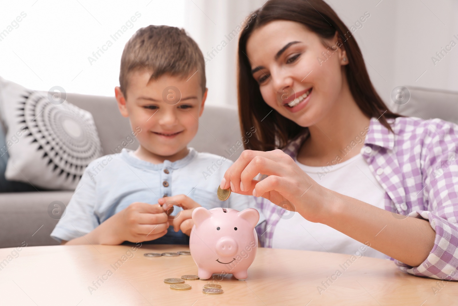 Photo of Happy mother and son putting coins into piggy bank at home