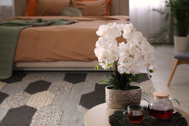 Photo of Beautiful white orchids and tea set on table in bedroom, space for text. Interior design