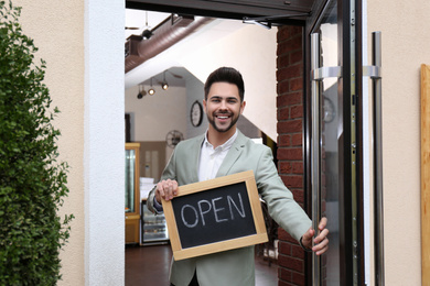 Photo of Young business owner holding sign OPEN at door of his cafe
