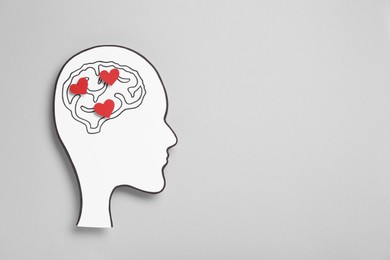 Photo of Emotional thinking. Paper human head cutout with drawing of brain and red hearts on grey background, top view. Space for text