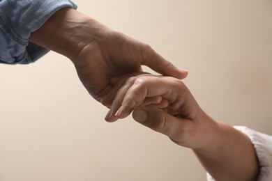 Woman holding hands with her mother on beige background, closeup