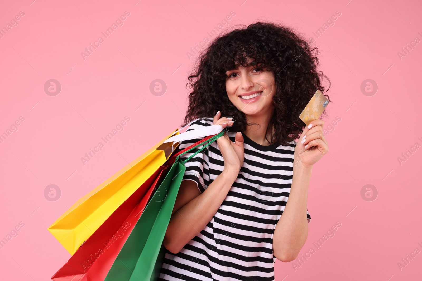 Photo of Happy young woman with shopping bags and credit card on pink background