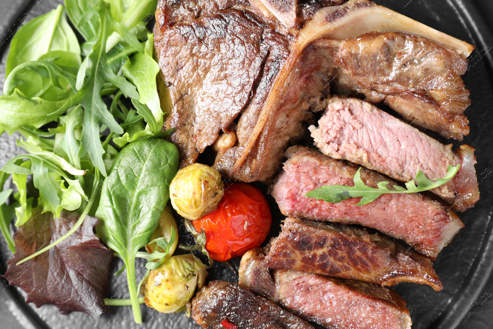 Photo of Delicious grilled beef meat, vegetables and greens on board, top view