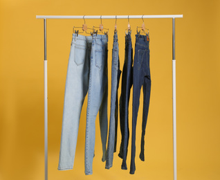 Photo of Rack with different jeans on yellow background