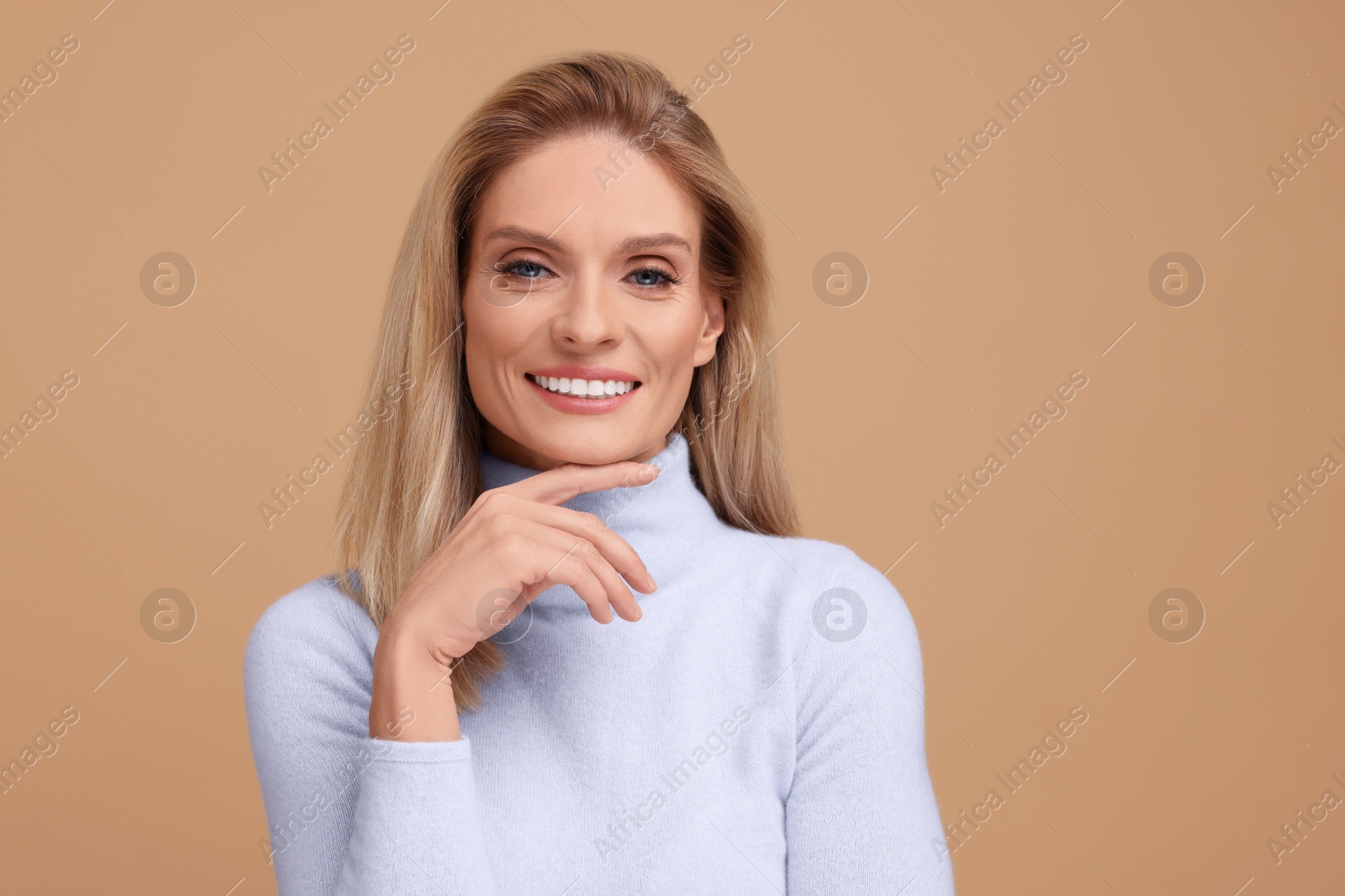 Photo of Portrait of smiling middle aged woman with blonde hair on beige background. Space for text