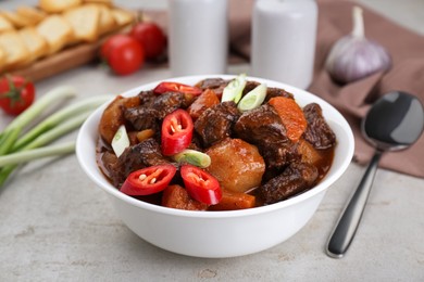 Photo of Delicious beef stew with carrots, chili peppers, green onions and potatoes on white textured table, closeup