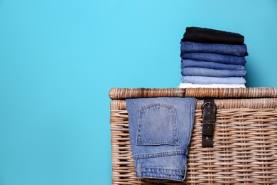 Photo of Stack of different jeans on basket against color wall with space for text