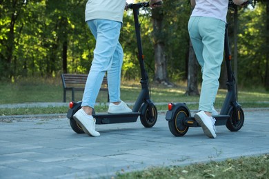 Couple riding modern electric kick scooters in park, back view