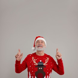 Photo of Senior man in Christmas sweater and Santa hat pointing at something on grey background
