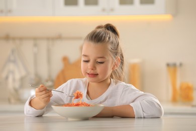 Photo of Cute little girl eating tasty pasta at table in kitchen