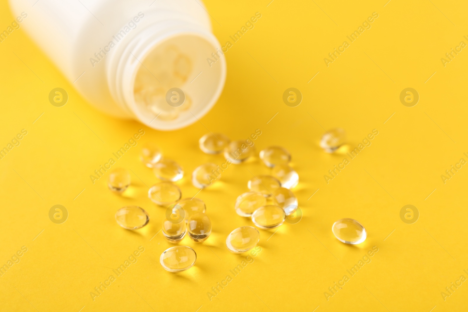 Photo of Vitamin capsules and medical bottle on yellow background, closeup