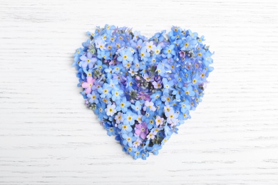 Photo of Heart made of forget-me-not flowers on white wooden background, top view