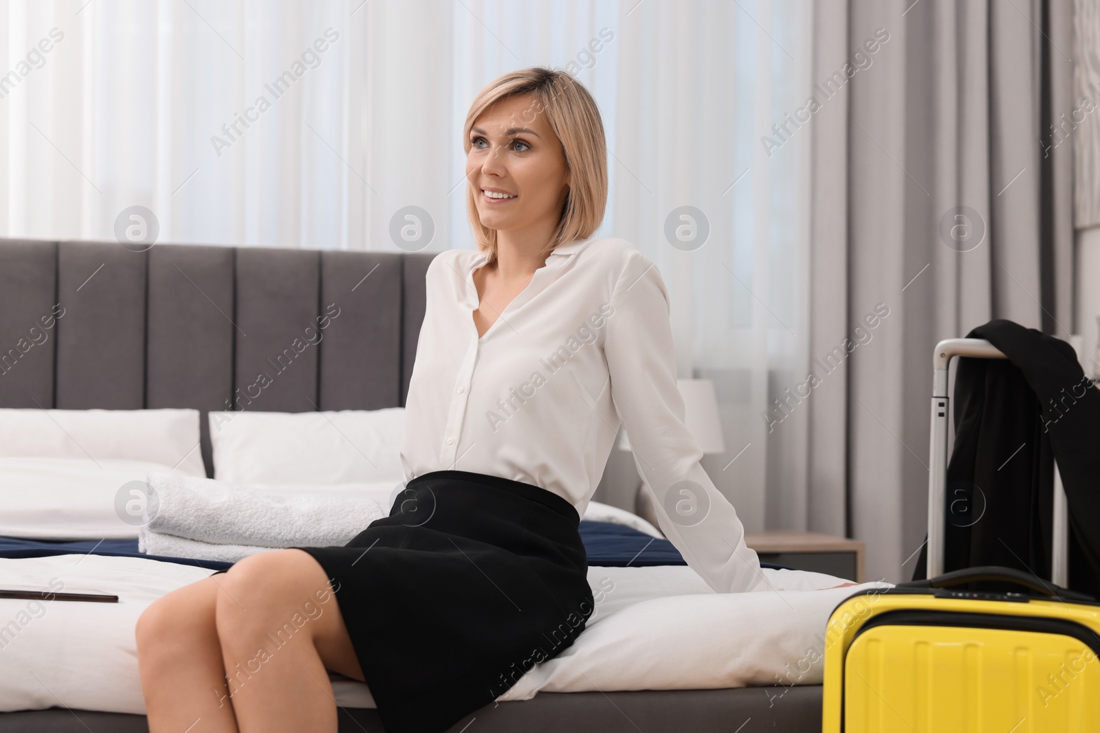 Photo of Smiling businesswoman relaxing on bed in stylish hotel room