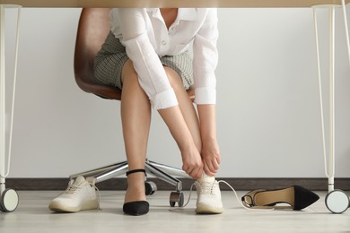 Photo of Woman taking off uncomfortable shoes and putting on sneakers in office, closeup