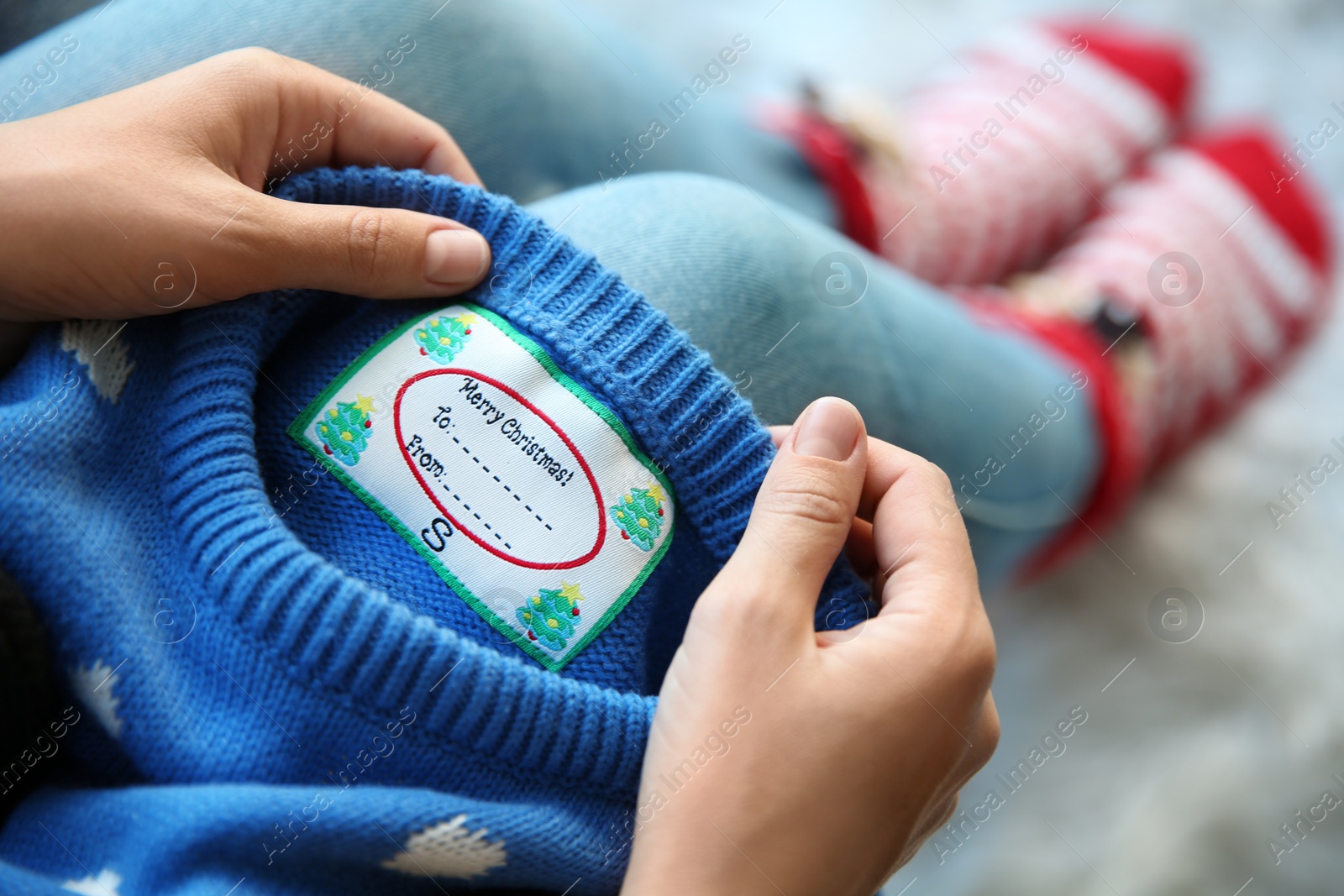 Photo of Woman holding Christmas sweater with tag, closeup