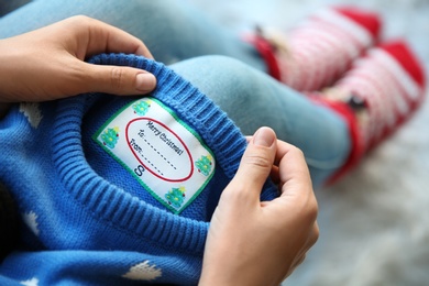 Photo of Woman holding Christmas sweater with tag, closeup