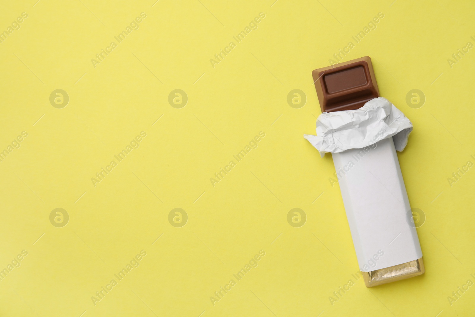 Photo of Tasty chocolate bar in package on light yellow background, top view. Space for text