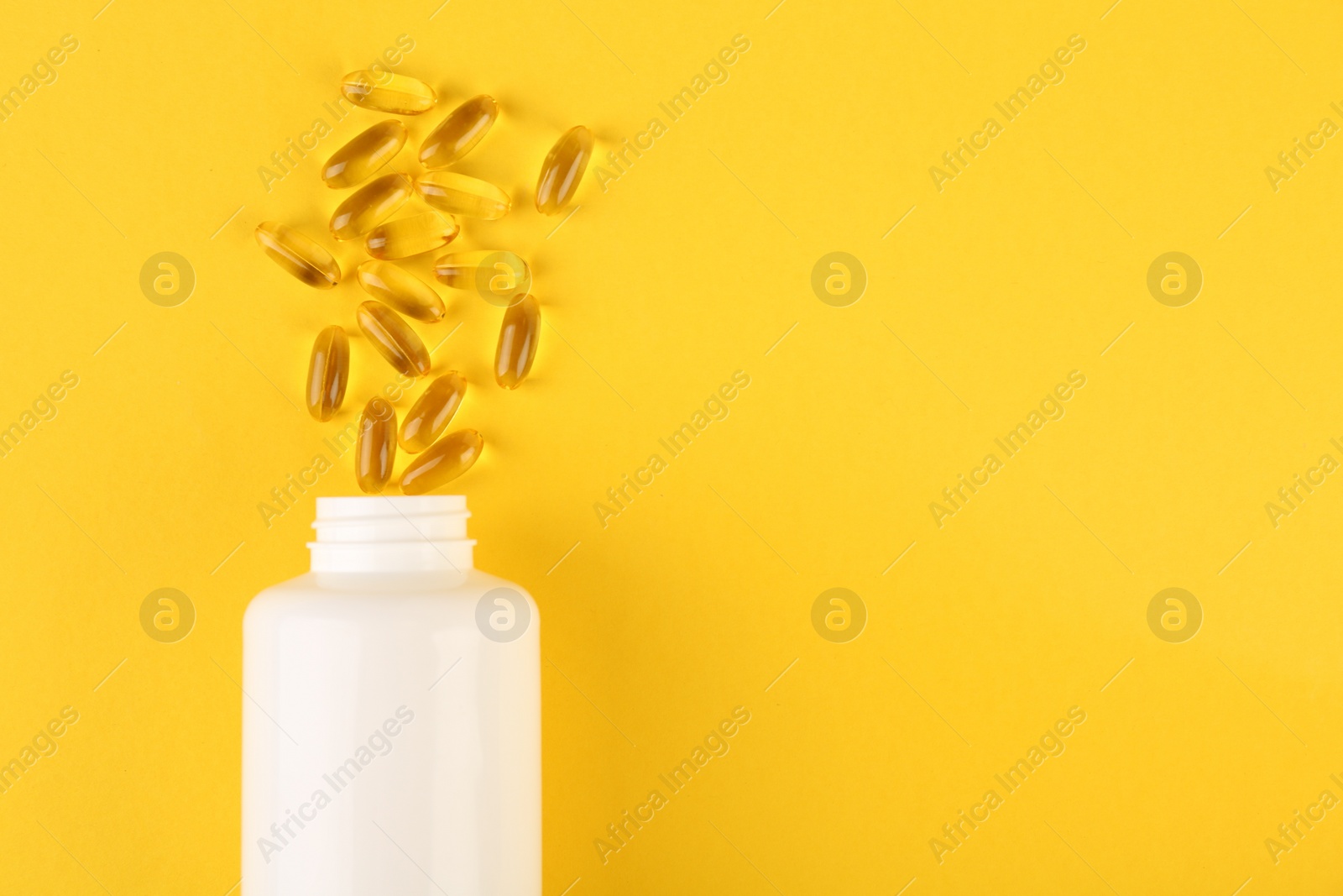 Photo of White medical bottle and vitamin capsules on yellow background, top view. Space for text