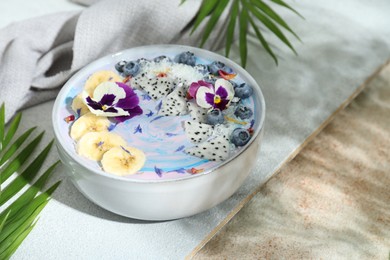 Delicious smoothie bowl with fresh fruits, blueberries and flowers on color textured table. Space for text