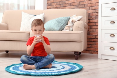 Photo of Cute little boy drinking milk on floor at home
