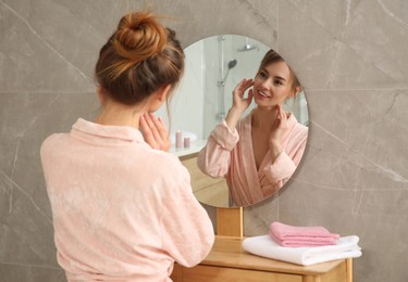 Photo of Beautiful woman wearing pink bathrobe in front of mirror at home