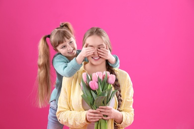 Happy mother and daughter with flower bouquet on color background. International Women's Day