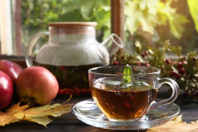 Photo of Hot tea, apples and dry leaves on wooden windowsill. Autumn atmosphere
