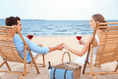 Photo of Happy young couple with glasses of wine sitting on deck chairs at sea beach