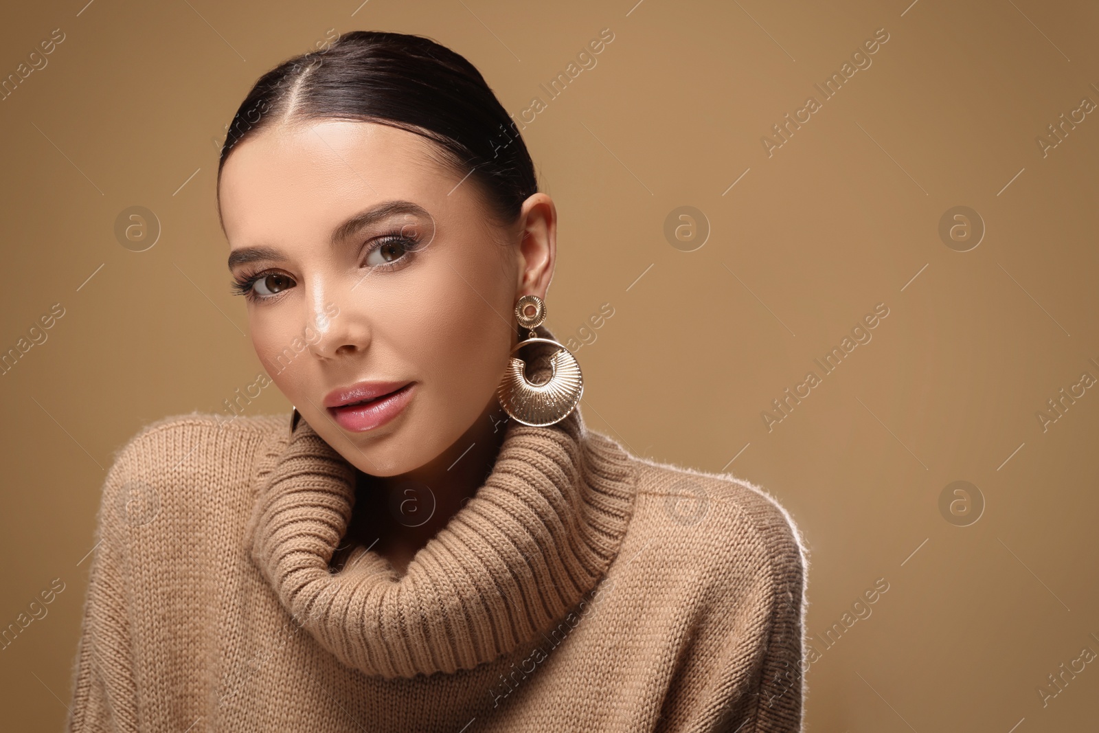 Photo of Beautiful young woman with elegant earrings on light brown background