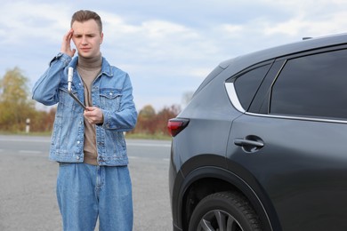 Worried young man near car with punctured wheel on roadside