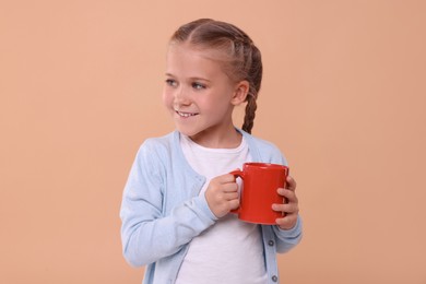 Photo of Happy girl with red ceramic mug on beige background