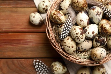 Photo of Speckled quail eggs and feathers on wooden table, flat lay. Space for text