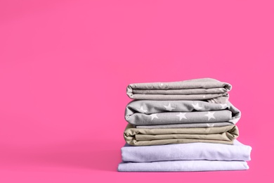 Photo of Stack of clean bed sheets on pink background. Space for text