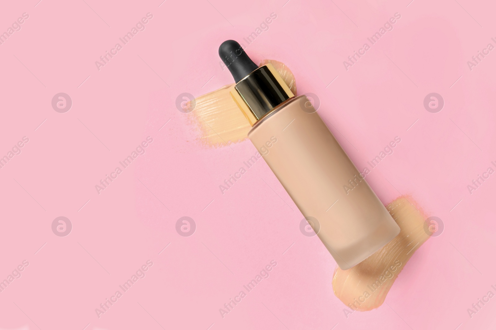 Photo of Liquid foundation and swatches on pink background, top view. Space for text