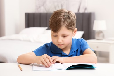 Photo of Little boy erasing mistake in his notebook at white desk indoors