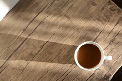 Photo of Cup of coffee on wooden table in morning, top view. Space for text