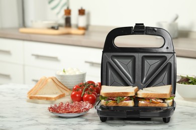 Photo of Modern grill maker with sandwiches and different products on white marble table in kitchen
