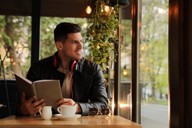 Man with headphones and book at table in cafe