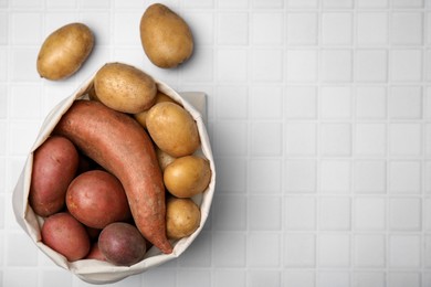 Photo of Different types of fresh potatoes in bag on white table, top view. Space for text