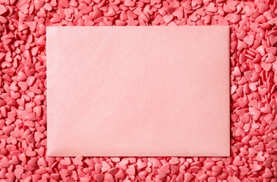 Photo of Blank card on pile of pink heart shaped sprinkles, top view. Space for text