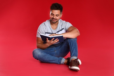 Photo of Handsome young man reading book on red background